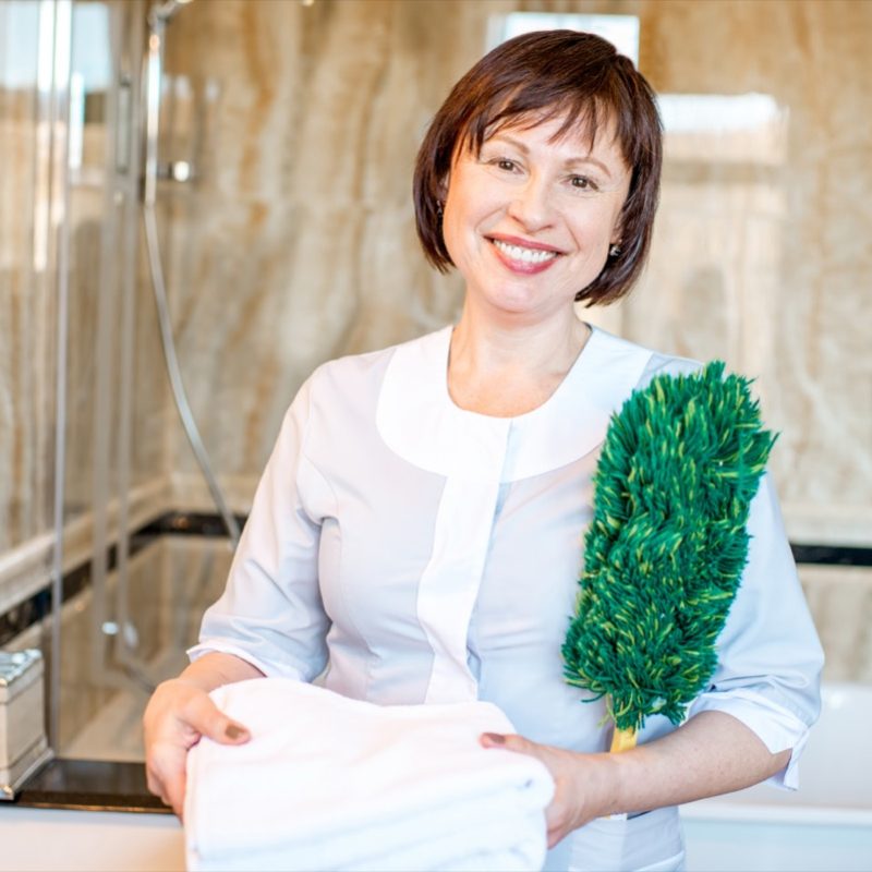 Portrait of a senior chambermaid standing with dust brush in the hotel bathroom